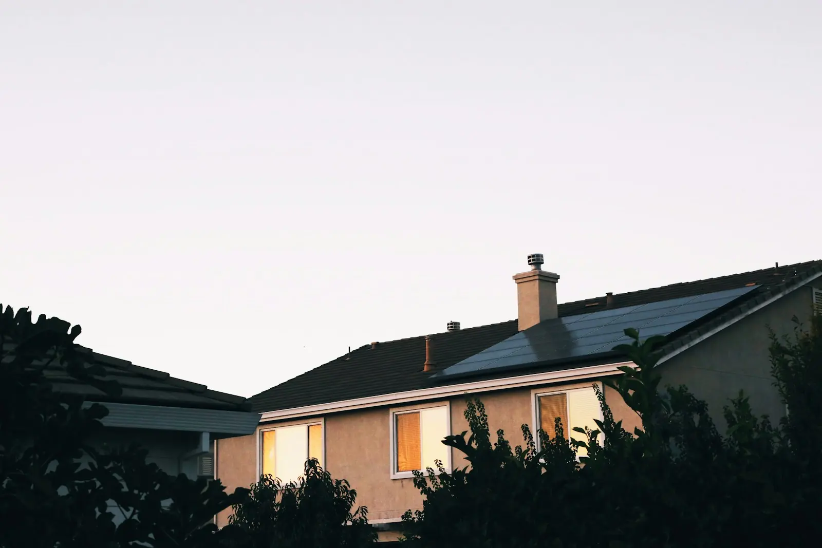 Einfamilienhaus in der Abenddämmerung, Solarmodule auf dem Dach, warmes Licht in den Fenstern