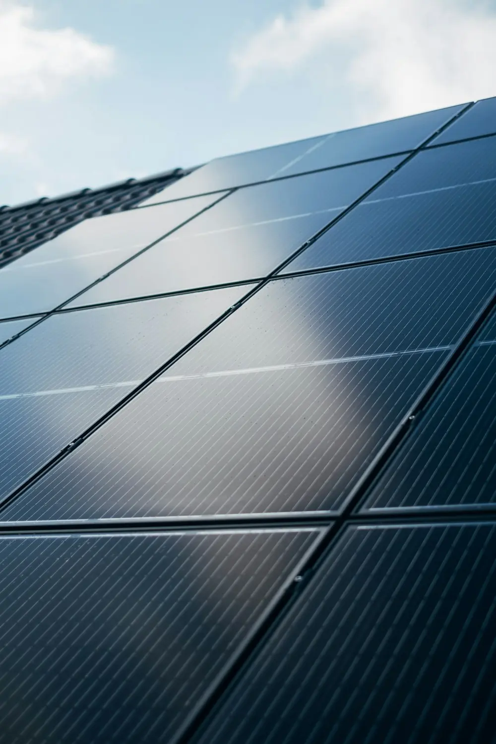 Nahaufnahme schwarzer Solarmodule auf einem Ziegeldach, im Glas spiegelt sich der Himmel