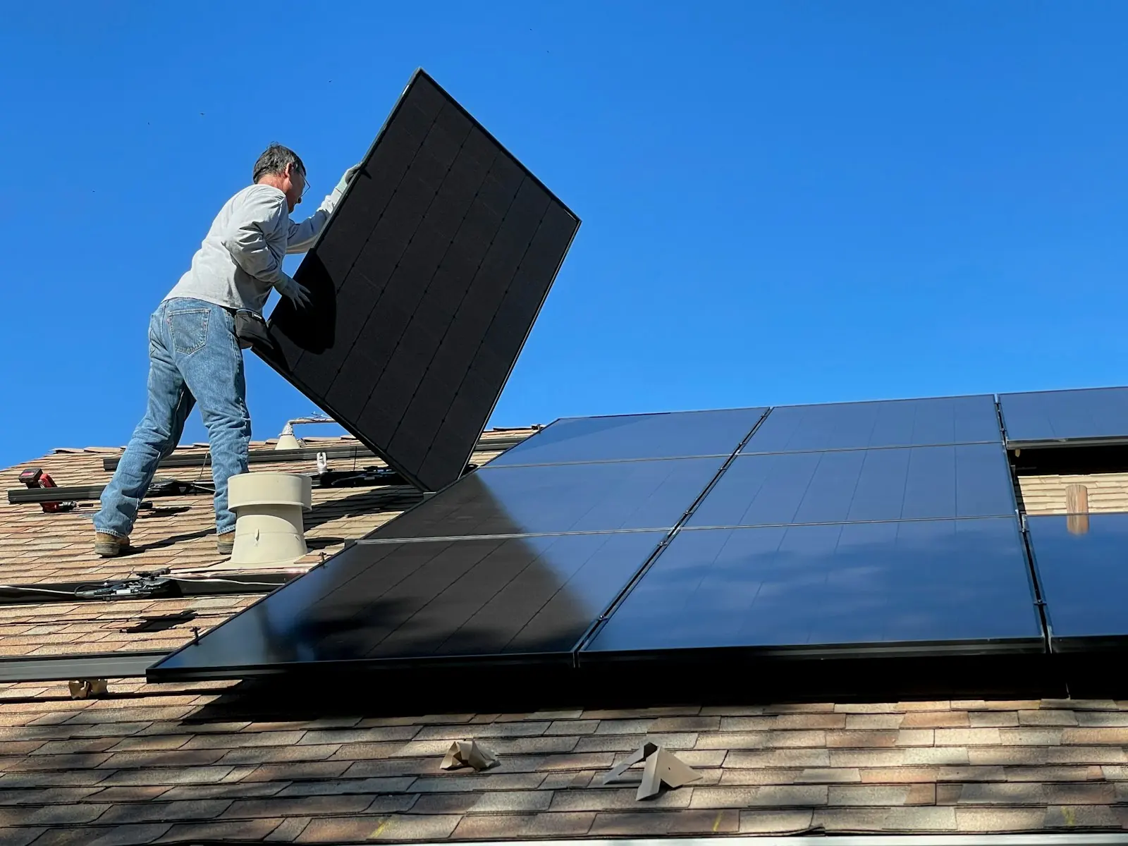 Monteur trägt ein schwarzes Solarmodul über das Dach, daneben bereits verlegte Module