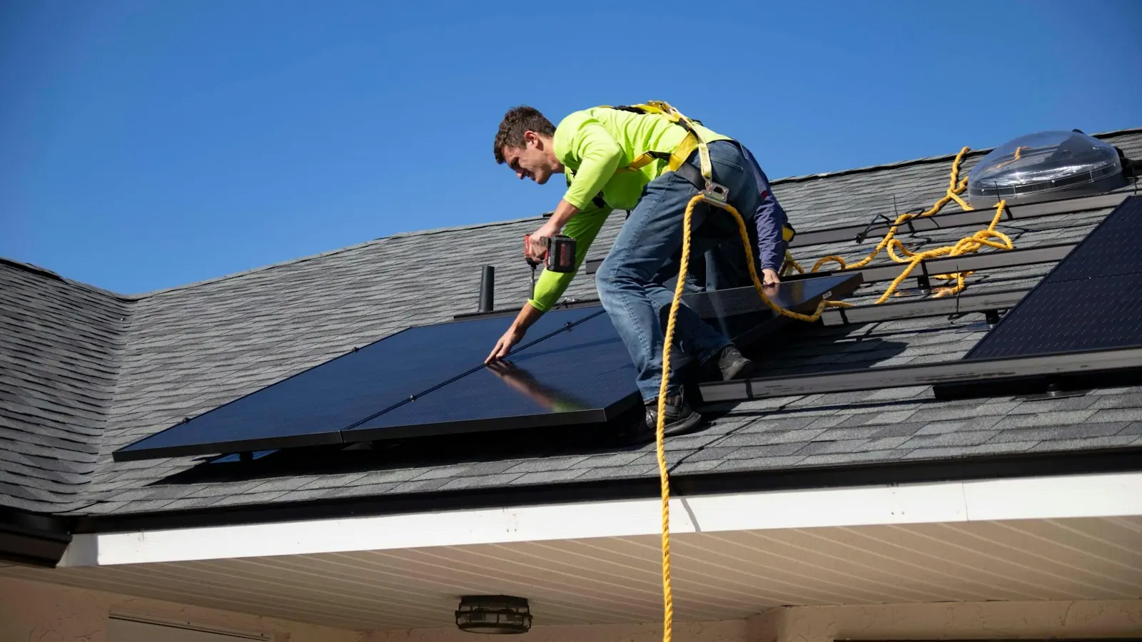 Monteur mit Sicherungsgurt verschraubt ein Solarmodul auf einem Schindeldach